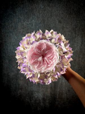 Vista dall'alto di un bouquet sposa con ortensie di carta rigida sfumata lilla e crema che circondano una rosa inglese rosa confetto.