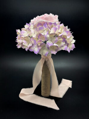 Profilo intero di un bouquet di carta con ortensie viola, impugnatura rivestita in corda naturale e un lungo fiocco in chiffon rosa antico.